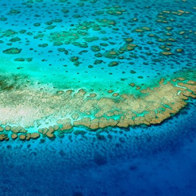 An aerial photo of turquoise and darker blue water around an area of the Great Barrier Reef. 